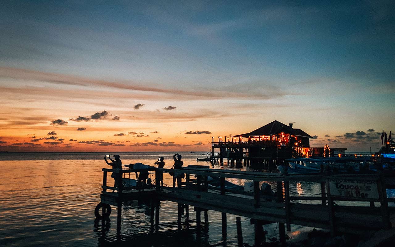 Tourists taking a photo of the colorful sky during a sunset in Roatan 