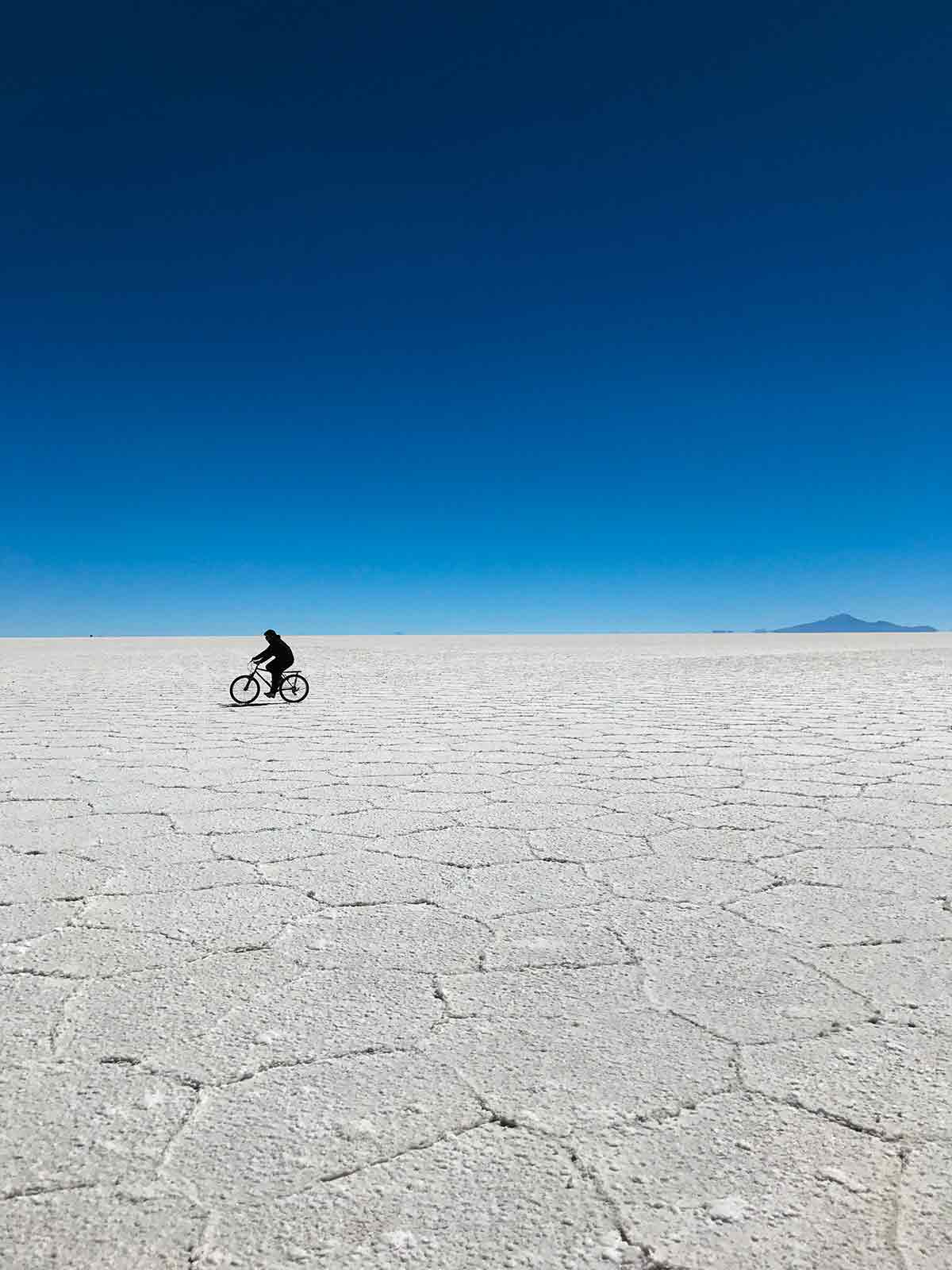 A man riding a bike  in the crystallized surface with hexagonal formations of Salar de Uyuni